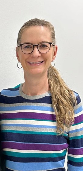 Woman, a gallup-certified strengths coach, scientific leadership coach at stand on strengths, standing with long curly hair and glasses