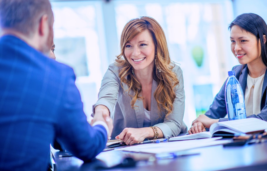 Two female hr professionals in business attire shake the hand of a male new hire